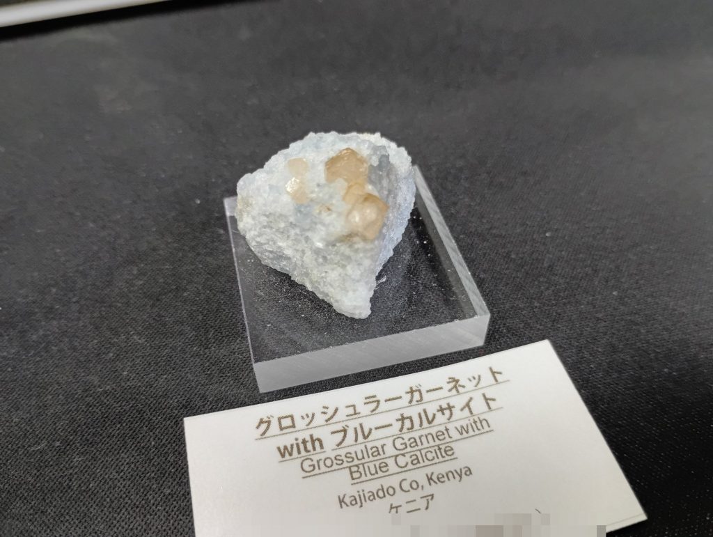 グロッシュラーガーネット with ブルーカルサイト。青みがかった母岩にオレンジ色の結晶がのる